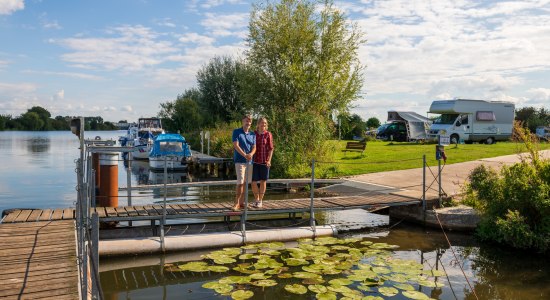 Et par står på en anløbsbro ved Weser-floden, i baggrunden en autocamper-parkeringsplads, © TMN / Markus Tiemann