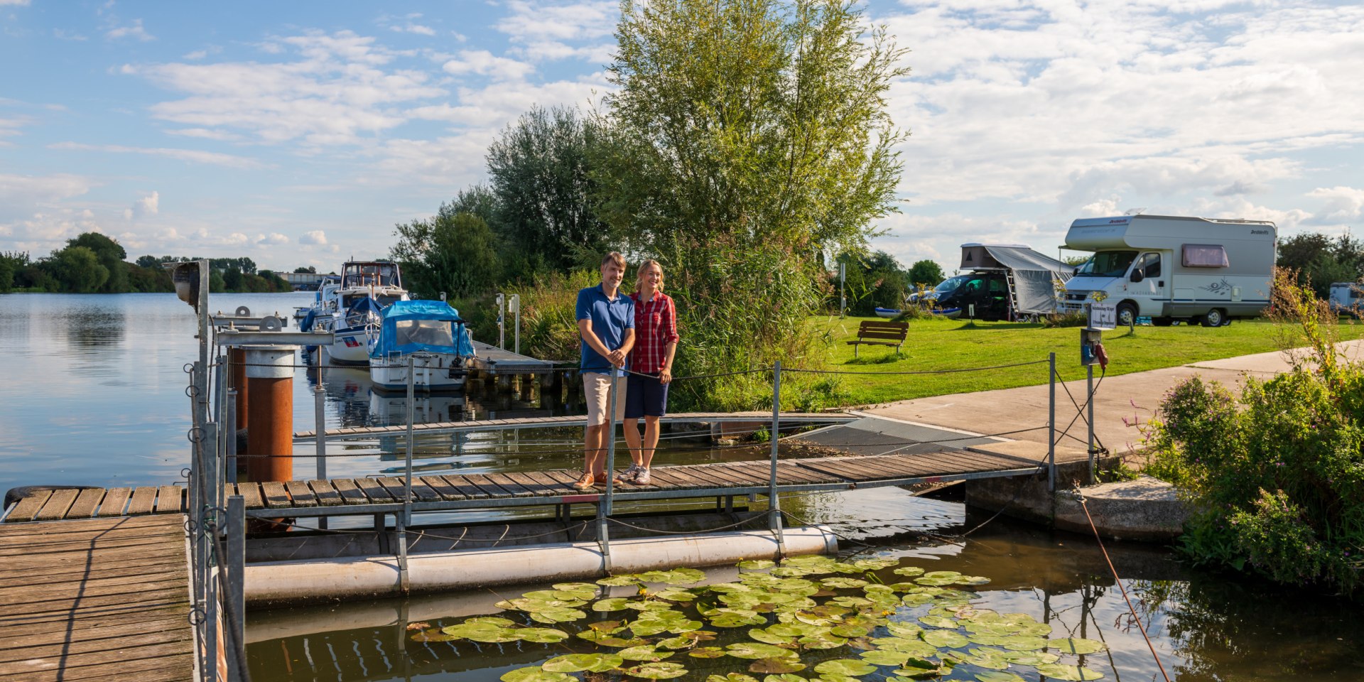 Et par står på en anløbsbro ved Weser-floden, i baggrunden en autocamper-parkeringsplads, © TMN / Markus Tiemann