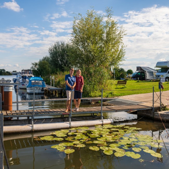 Et par står på en anløbsbro ved Weser-floden, i baggrunden en autocamper-parkeringsplads, © TMN / Markus Tiemann